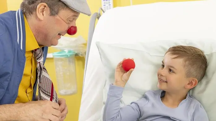 Man sieht einen Clown am Krankenhausbett eines Kindes, das lächelt