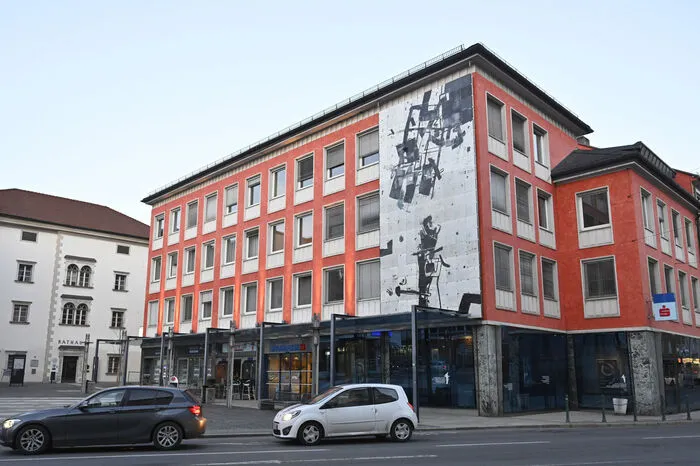 Die grelle orange Farbe weicht einem eleganten hellem Grauton, der sich an dem Rathaus und dem Schloss Porcia orientiert. Das Hoke-Kunstwerk bleibt auf der Fassade.