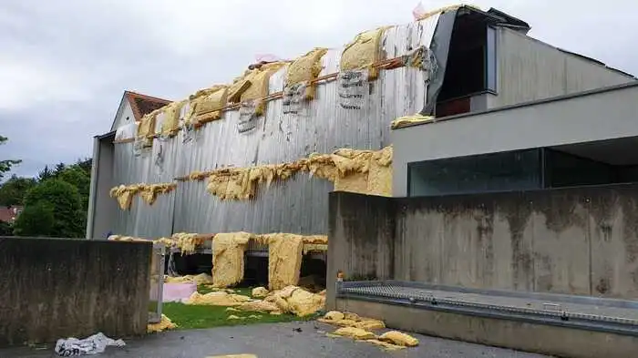 Heftige Sturmböhen haben fast das komplette Blechdach vom Turnsaal der Volksschule Flöcking heruntergerissen, Dämmmaterial liegt auf der Wiese verstreut.
