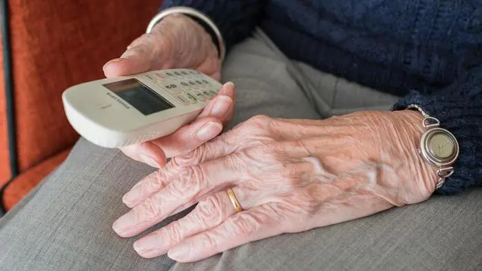Das Bild zeigt die Hände einer älteren Person, die ein Telefon in der Hand hält