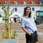 Chrissi Buchmasser steht mitten am Platz und lächelt verschmitzt in die Kamera, die Hände lässig in die Hosentaschen gesteckt
