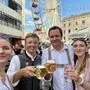 Vier Personen in Tracht sind auf einem Festgelände und lächeln in die Kamera, die zwei Männer in der Mitte prosten sich mit Bier zu