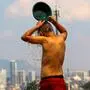 Ein Bursche mit freiem Oberkörper steht mit dem Rücken zum Betrachter und schüttet sich eine Schale mit Wasser über den Kopf, im Hintergrund erkennt man die Skyline einer Stadt