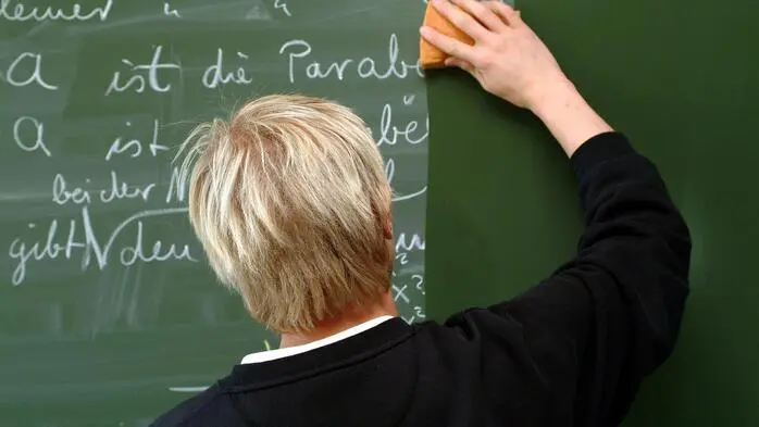 Das Bild zeigt einen Lehrer, der die Tafel putzt