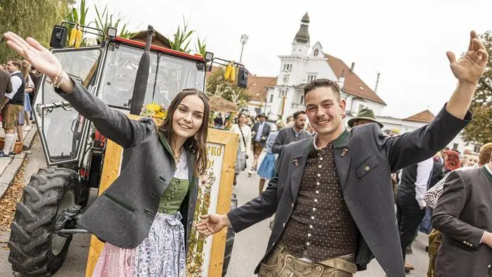 Ein Mann und eine Frau in Tracht stehen vor einem Traktor, der vor einem Bahnhof steht.
