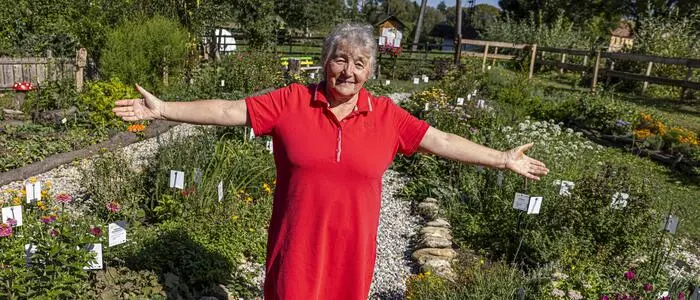 Eine Dame im roten Kleid streckt inmitten eines Kräutergartens ihre Hände aus