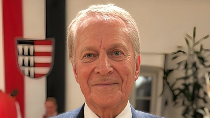 Ein Mann im Anzug und grauen Haaren lächelt verschmitzt in die Kamera