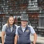 Eine junge Dame und ein Herr mit einem Filzhut stehen vor einer Almhütte