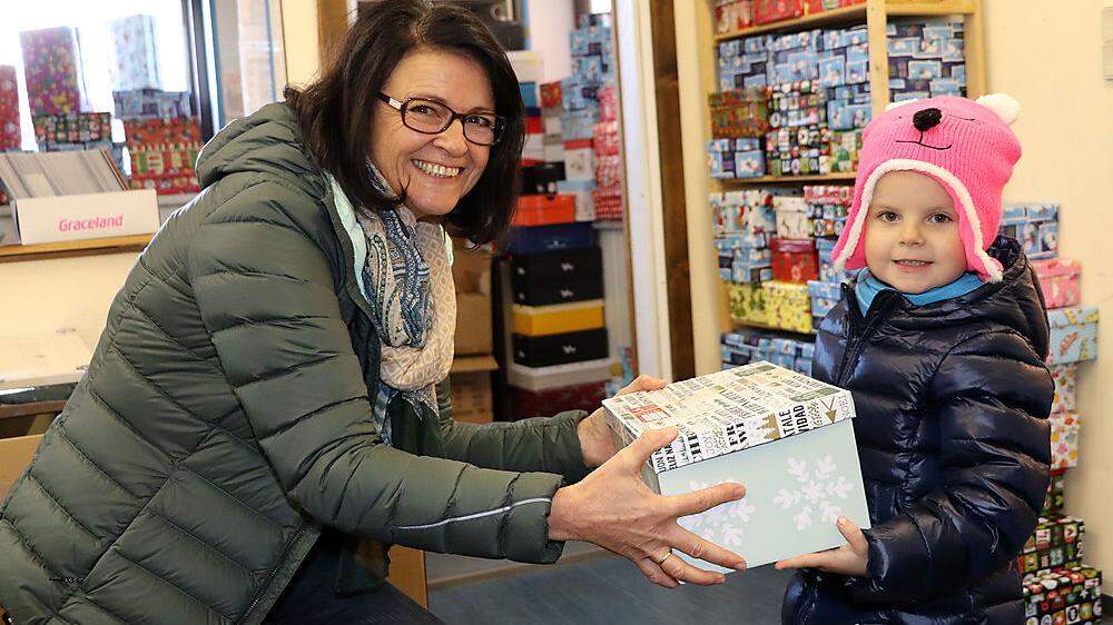 Ein Kindergartenkind übergibt Dagmar Preiml einen Schuhkarton für die Aktion &quot;Weihnachten im Schuhkarton&quot;