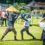 Zwei Personen in einer Fechtausrüstung machen auf einem Sportplatz einen Schwertkampf an einem sonnigen Tag