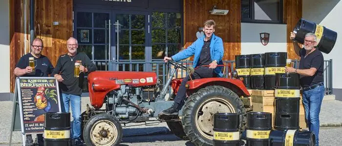 Vier Männer auf einem Oldtimer-Traktor und Bierfässern