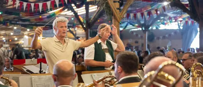 Ein Mann mit weißen Haaren dirigiert eine Blasmusik