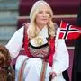 Kronprinzessin Mette-Marit sitzt in traditioneller Kleidung. Ihre rechte Hand liegt auf einem Hund, links hält sie die norwegische Flagge.