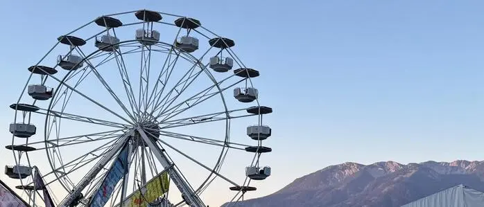 Ein Riesenrad, dahinter die Berge und Sonnenaufgang