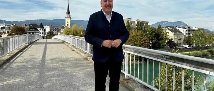 Ein Mann im Anzug auf einer Brücke, die Villacher Innenstadt im Hintergrund