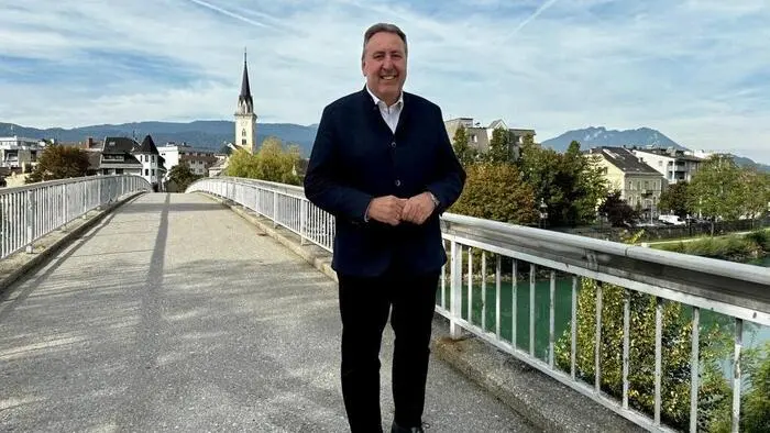 Ein Mann im Anzug auf einer Brücke, die Villacher Innenstadt im Hintergrund