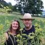Eine Frau und ein Mann stehen hinter Blumen und lachen in die Kamera