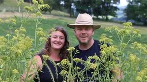 Eine Frau und ein Mann stehen hinter Blumen und lachen in die Kamera