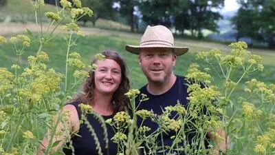 Eine Frau und ein Mann stehen hinter Blumen und lachen in die Kamera