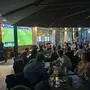 Viele Menschen sitzen in einem Gastgarten und verfolgen ein Fußballspiel im Fernsehen