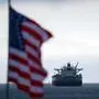 Eine US-Flagge im Vordergrund und ein Öltanker dahinter.