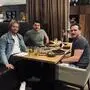 Drei Männer sitzen in einem Restaurant am Tisch, der gedeckt ist und lächeln in die Kamera