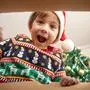 Happy surprised Caucasian little boy in Santa's hat looking inside a cardboard box, at home near Christmas tree, bottom view. Excited little kid opening Christmas present. 