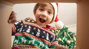 Happy surprised Caucasian little boy in Santa's hat looking inside a cardboard box, at home near Christmas tree, bottom view. Excited little kid opening Christmas present. 