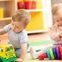 Kids playing with educational toys. Children sit on a rug in a play room at home or kindergarten. Toddler boy with toy lorry and baby girl with rings.