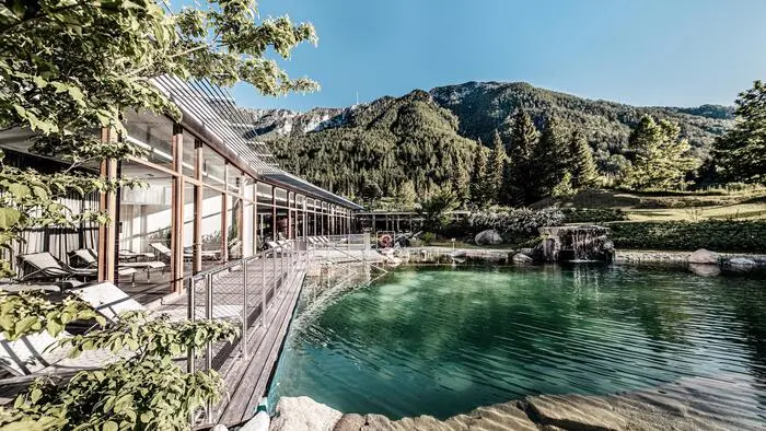 Blick auf einen Teich in einer Wellnessanlage, dahinter erheben sich Berge