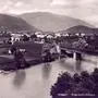 Schwarz-Weiß-Aufnahme: Ein Fluss mit Brücke, dahinter Felder, Häuser und Berge | Villach Lind im Jahr 1920