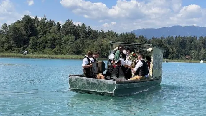 Ein kleines Boot mit mehreren Menschen in Trachtenoutfits auf einem See