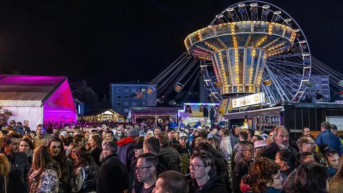 Ein abendliches Überblicksbild mit vielen Besuchern und beleuchteten Zelten und Fahrgeschäften:
