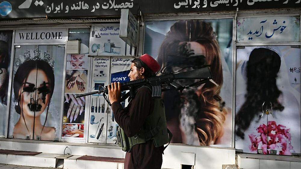 Ein Taliban-Kämpfer geht an einem Schönheitsssalon in Kabul vorbei - die Bilder der Gesichter der Frauen wurden besprayt