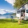 Ein Camping-Van mit Zeltaufbau steht am Seeufer, wo zwei Camper frühstücken | Van-Camping ist vor allem bei Jüngeren sehr beliebt