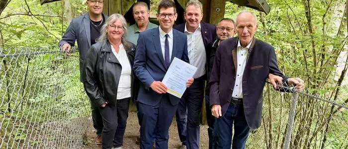 Mehrere Menschen stehen auf einem Waldweg vor einer Hütte, links und rechts ist ein Zaun