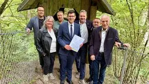 Mehrere Menschen stehen auf einem Waldweg vor einer Hütte, links und rechts ist ein Zaun