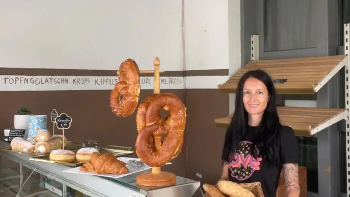 Eine dunkelhaarige Frau steht hinter einem Bäckereiverkaufstresen und lächelt in die Kamera