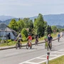 Viele Radfahrer fahren auf einer Straße, im Hintergrund sind Berge und ein See