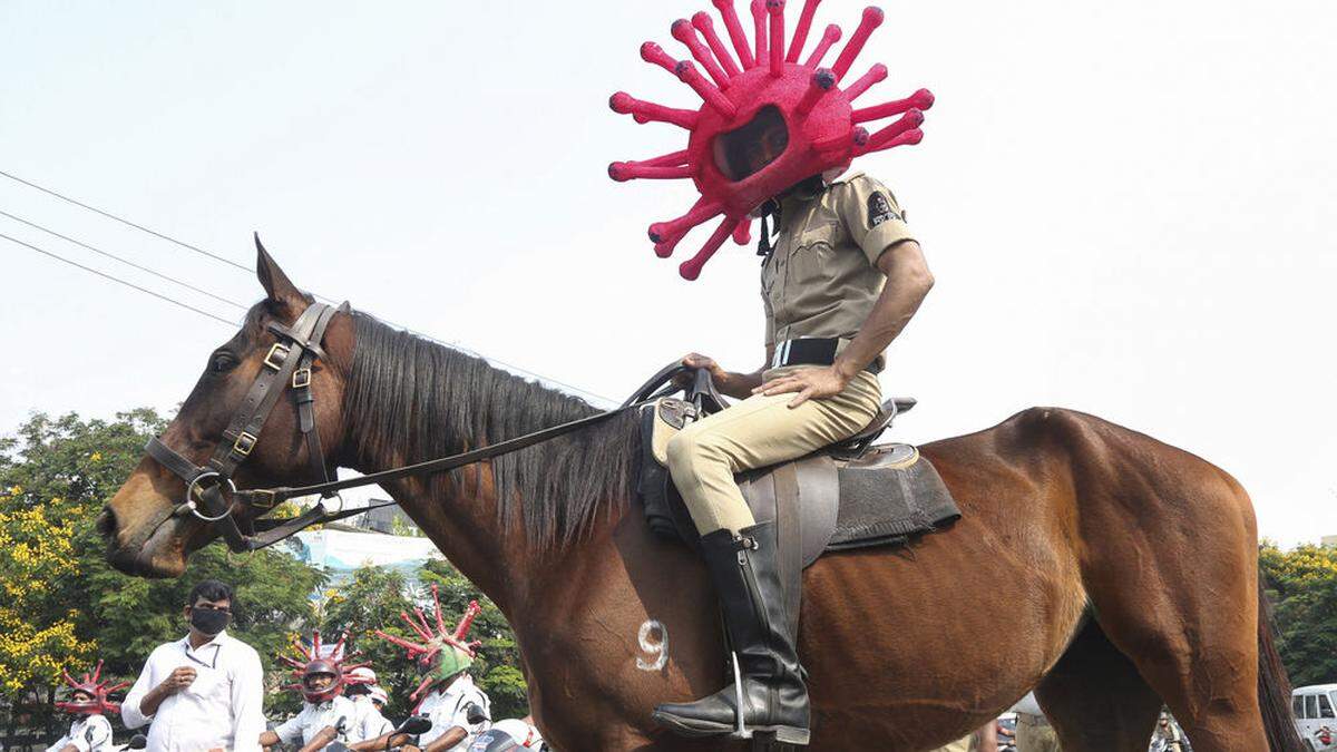 Mit einem Helm, der aussieht wie das Corona-Virus, hält ein Polizist in Indien Menschen an und ermahnt sie, zu Hause zu bleiben. 