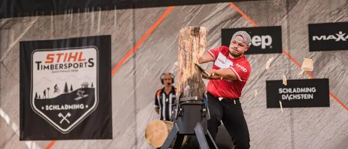 Ein Mann hackt auf einer Bühne mit einer Axt auf ein Stück Holz ein