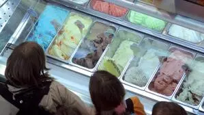 Eisdiele mit mehreren Sorten Eis von oben und drei Menschen, die auf die Vitrine blicken