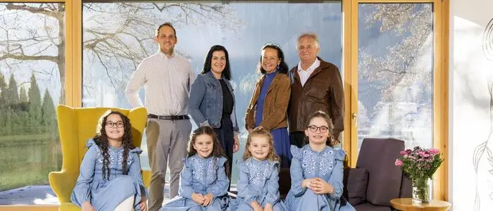 Familienfoto: in erster Reihe sitzen vier Mädchen in blauen Kleidern, dahinter stehen die Eltern und Großeltern