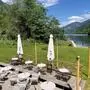 Ein Gastgarten auf einer Wiese, im Hintergrund ein See und Berglandschaft
