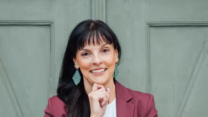 Eine Frau in einem bordeauxfarbenen Blazer lacht in die Kamera