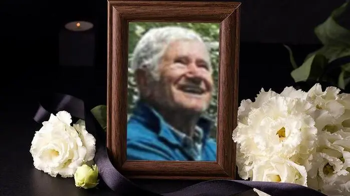 Ein Foto von einem älteren Mann in einem Bilderrahmen, daneben liegen weiße Blumen