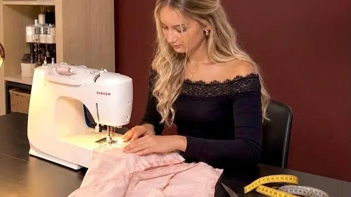 Eine junge Frau sitzt an einer Nähmaschine in ihrem Atelier und näht ein Kleidungsstück