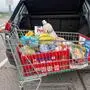 Ein prall gefüllter Einkaufswagen steht vor einem Auto, bei dem der Kofferraum geöffnet ist