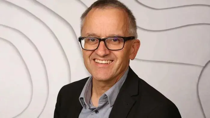 Porträt eines älteren Mannes mit Brille und Hemd. Er lächelt in die Kamera
