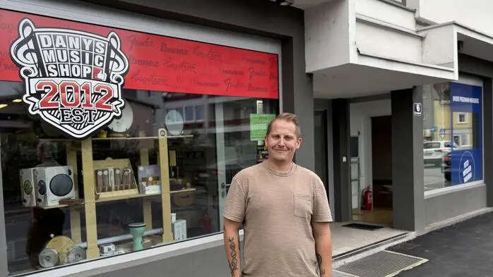 Ein Mann steht vor einem Musikgeschäft und lächelt in die Kamera